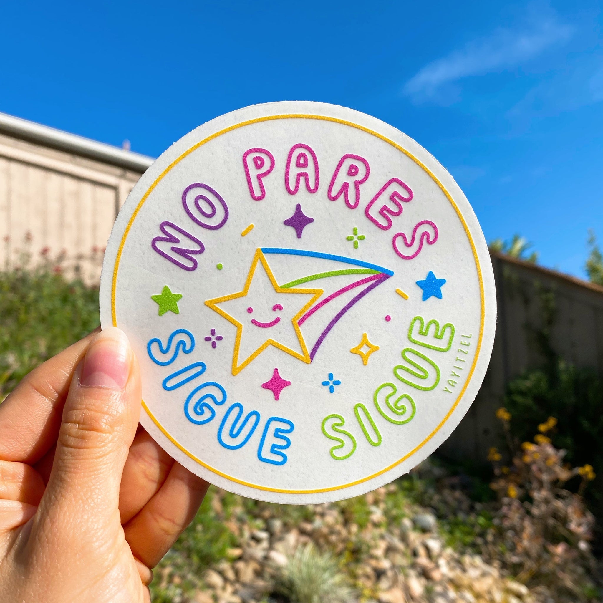 circle shape suncatcher with shooting star in the middle winking and with the phrase "no pares sigue sigue" around it