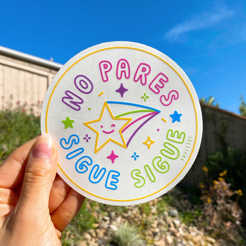 circle shape suncatcher with shooting star in the middle winking and with the phrase "no pares sigue sigue" around it