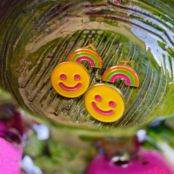 Smiley and rainbow earrings sitting on a ceramic dish bowl